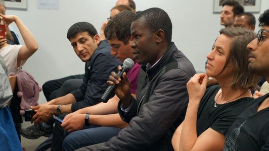 People sitting arranged in a row and one man speaking into a microphone