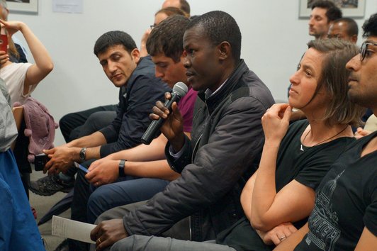 People sitting arranged in a row and one man speaking into a microphone