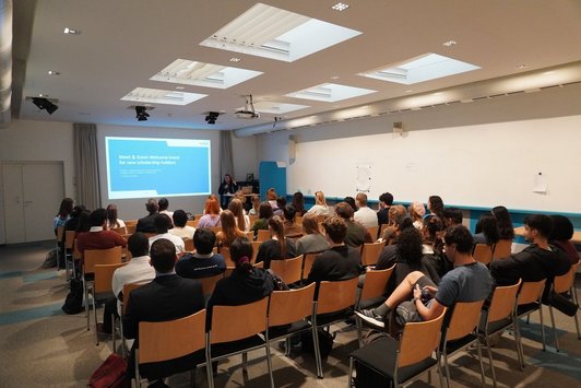 Room with participants sitting in rows, looking at a presentation slide and listening to a speaker