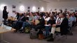 A man is giving a speech in front of an audience of approximately 50 people.