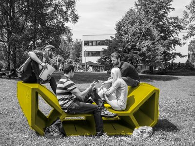 Studierende auf einem Enzi-Möbel im Garten der Universität Klagenfurt