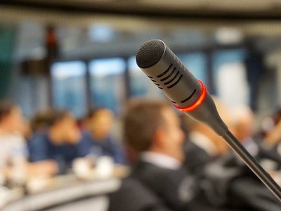 Mikrofon in Hörsaal. Der Fokus ist auf der Großaufnahme vom Mikrofon, während der Seminarraum dahinter verschwommen ist.