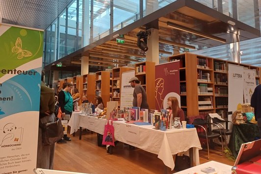 Messebesucher:innen an Ständen vor Bücherregalen