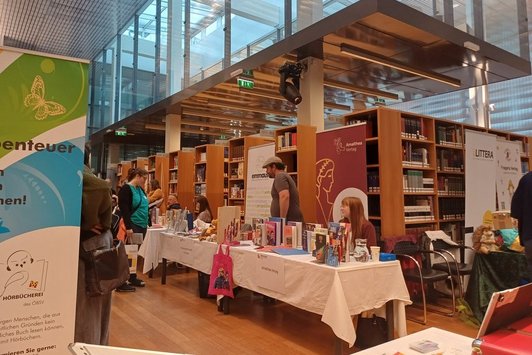 Messebesucher:innen an Ständen vor Bücherregalen