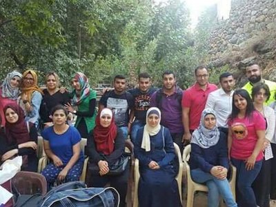 Group of people posing for a picture in frint of stone wall and trees