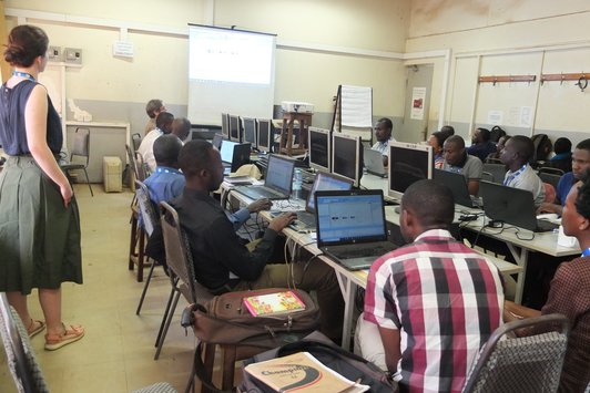 Group of people sitting at their workplaces and one woman standing in their background