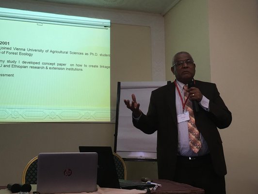 Man with microphone standing in front of his presentation on a wall in a darkened room 