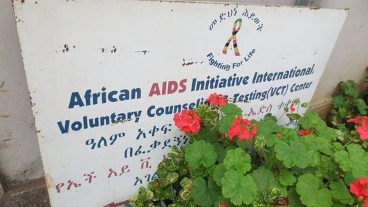 White sign with blue and red written information and a logo on it standing next to some flowers