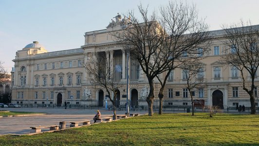 Außenansicht des Gebäudes der Iwan Franko Universität in Lemberg. Vor dem Gebäude stehen Bäume, Wiesen und Parkbänke.