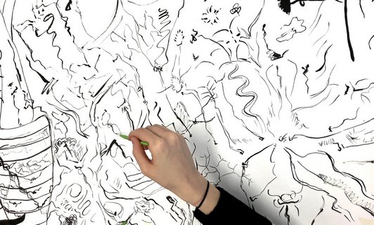 Eine Hand ist im Bild zu sehen, sie hält einen dünnen Pinsel und mal abstrakte Formen auf weißen Hintergrund