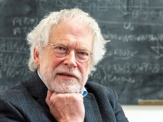 Ein Bild eines Mannes mit weißen Haaren und weißem Bart, der seinen Kopf auf seiner Faust ablegt.