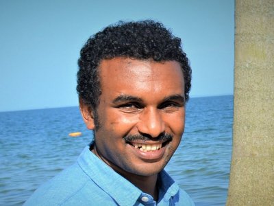 A man standing beside a tree and in front of what looks like the ocean.