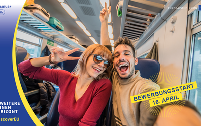 Eine junge Frau und ein junger Mann sitzen im Zug und machen ein Selfie