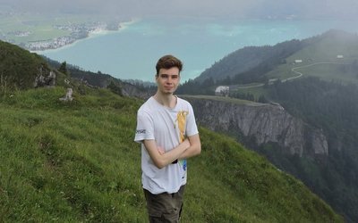 Ernst Mach Ukraine Stipendiat Ivan Solovei steht auf einem Berg, hinter ihm eine weite Aussicht auf die Landschaft und einen See im Tal