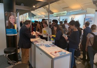 Ein Mitarbeiter des OeAD berät Schülerinnen und Schüler am Messestand.