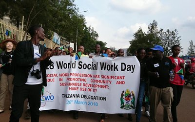 Gorup of people with a big white flag with information on the 28. World Social Work Day on it walking on the streets