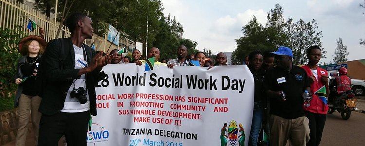 Gorup of people with a big white flag with information on the 28. World Social Work Day on it walking on the streets