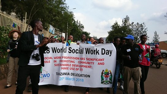 Gorup of people with a big white flag with information on the 28. World Social Work Day on it walking on the streets