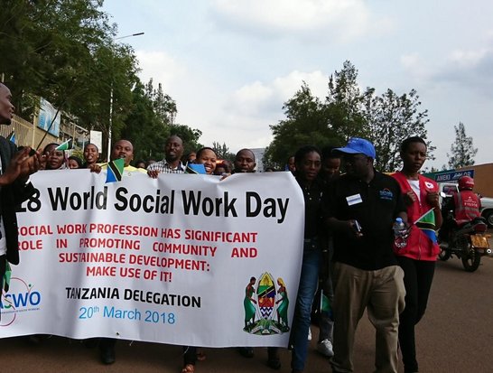 Gorup of people with a big white flag with information on the 28. World Social Work Day on it walking on the streets