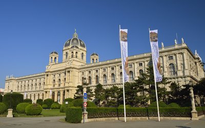Das naturhistorische Museum Wien von Außen mit zwei wehenden Fahnen im Wind und blauem Himmel.