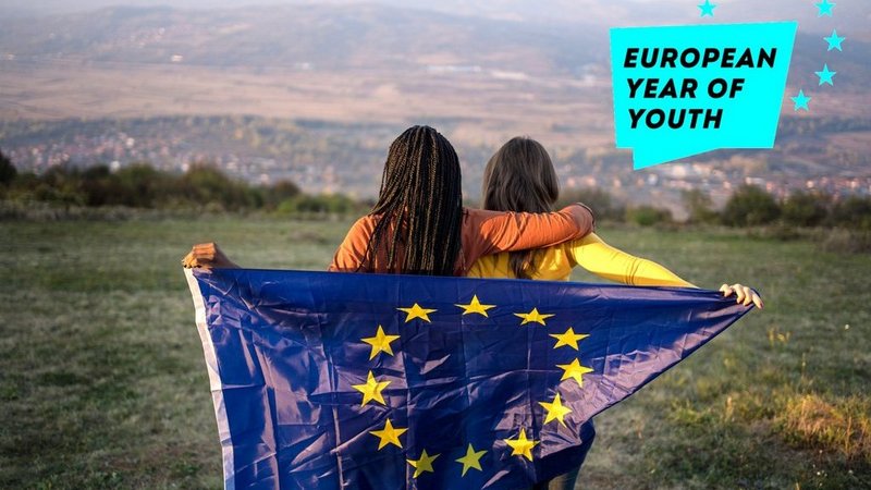Zwei junge Frauen halten gemeinsam die EU Flagge hinter ihrem Rücken und schauen in die Ferne