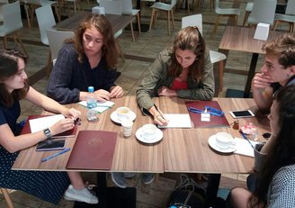 Fünf Studentinnen sitzen rund um einen Tisch und arbeiten an ihrem Projekt.