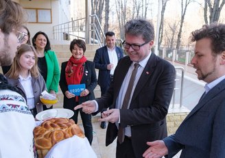 Ein junger Mann überreicht dem österreichischen und dem moldauischen Bildungsminister ein traditionelles lokales Gebäck, das aussieht wie ein Germzopf