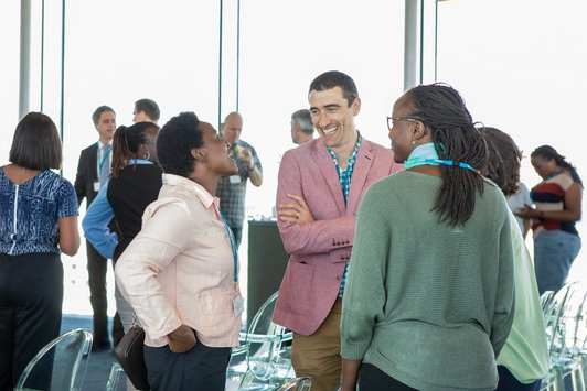 Networking in der Pausenzeit: Zwei Frauen und ein Mann unterhalten sich gemütlich vor einer Glaswand mit Ausblick auf Wien