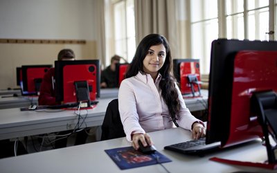 Mädchen sitzt in einer Schule vor einem Computer und sieht in die Kamera