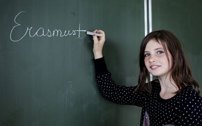 Mädchen schreibt mit Kreide Erasmus+ auf Schultafel