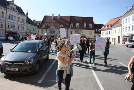 Group of people holding up posters with slogans and one woman speaking through a megaphone