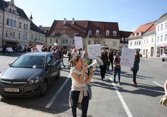 Group of people holding up posters with slogans and one woman speaking through a megaphone