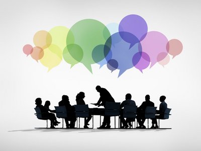 Grafik mit einer Gruppe von Menschen, die an einem Tisch sitzen und diskutieren. Über ihren Köpfen sind bunte Sprechblasen zu sehen.