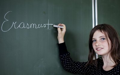 Mädchen schreibt mit Kreide das Wort Erasmus auf eine Schultafel.