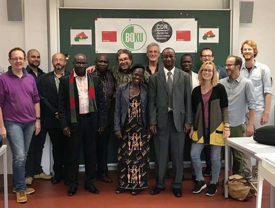Group of people posing in front of a blackboard with a project poster on it