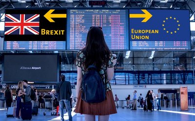 Rückenansicht einer jungen Frau auf einem Flughafen. Auf den Tafeln sind zwei Schilder mit den Aufschriften "Brexit" und "Europäische Union" zu sehen. 