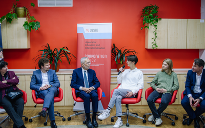Der österreichische Bundespräsident Alexander Van der Bellen sitzt mit Schülern und Schülerinnen und politischen Vertretern in einem Stuhlkreis vor einer rot bemalten Wand