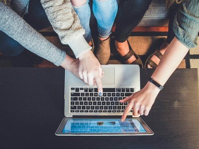 Menschen um einen Laptop zeigen mit Fingern auf Bildschirm