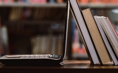 Laptop aufgeklappt und Bücher vor Bücherregal