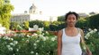 Kasha Tadel Gebre, in a white T-shirt, stands in front of a park with white flowers and a magnificent building in the background. 