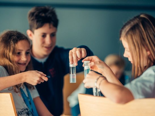 Zwei Schülerinnen und ein Schüler sitzen und betrachten eine Flüssigkeit