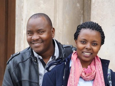 A woman and a man are standing in front of a house and smiling into the camera.