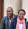 A woman and a man are standing in front of a house and smiling into the camera.