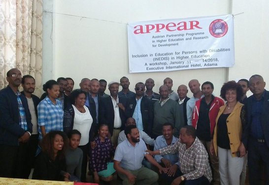 Group of people posing for a picture under a big APPEAR poster