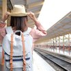 Frau mit Strohhut und Rucksack wartet am Bahnsteig