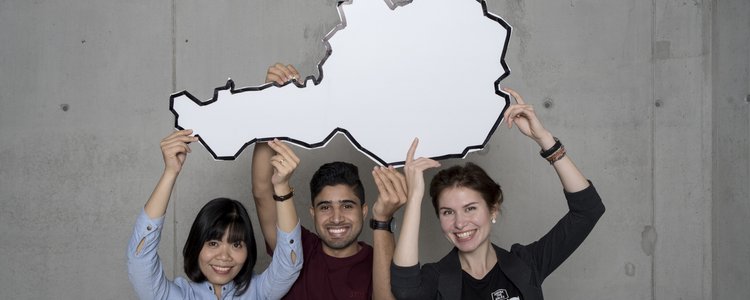 3 internationale Studierende halten eine Österreich-Karte in die Luft