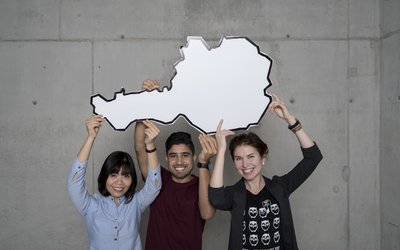 3 internationale Studierende halten eine Österreich-Karte in die Luft