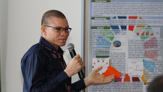 Vincent-Paul Sanon talking into a microphone with a poster next to h im