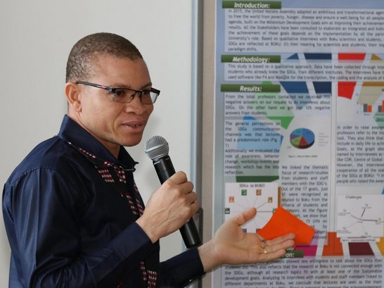 Vincent-Paul Sanon talking into a microphone with a poster next to h im