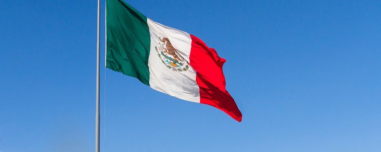 Eine mexikanische Flagge weht im Wind im Hintergrund der klare blaue Himmel.